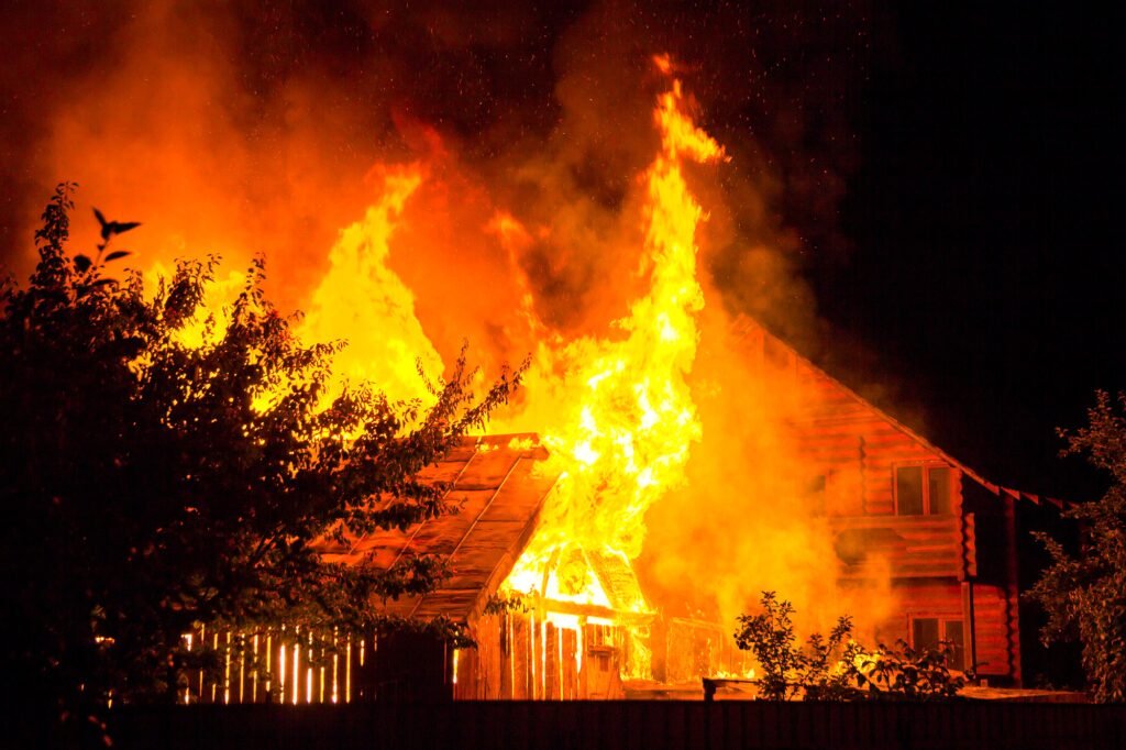 Burning wooden house at night. Bright orange flames and dense smoke